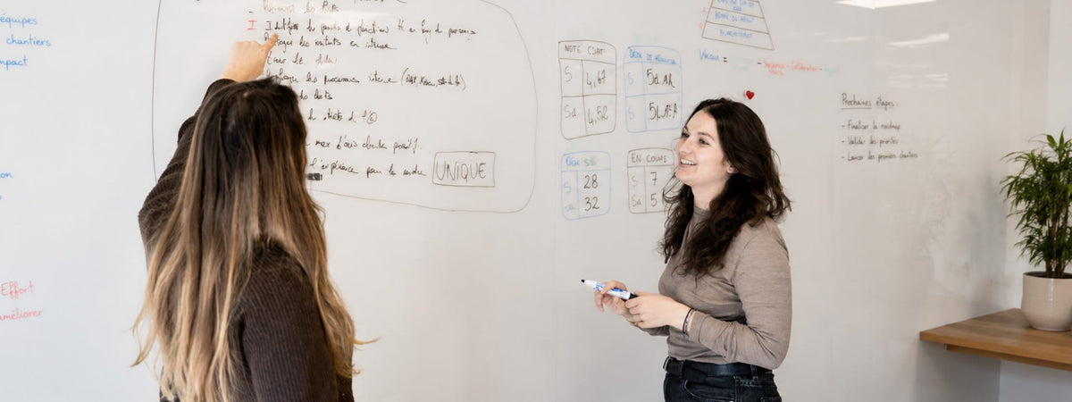 Deux collaboratrices en réunion devant un grand tableau blanc mural dans un bureau lumineux et moderne – Maison Pavane