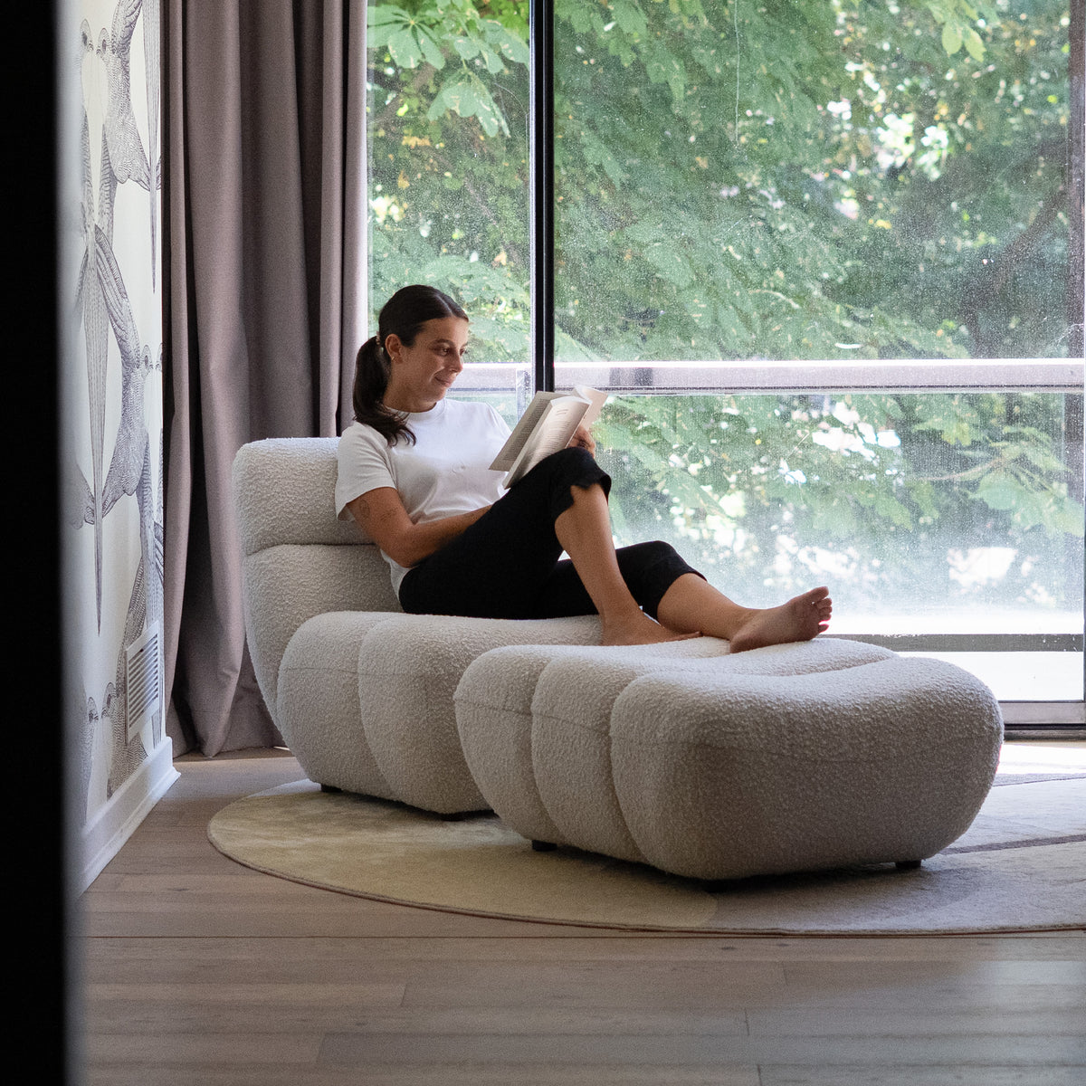 Fauteuil et repose-pied tissu bouclé blanc avec femme dessus grande baie vitrée – Maison Pavane