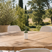 Petite lampe nomade Elo en plastique vert olive, posée sur une table en bois d'une terrasse à la campagne